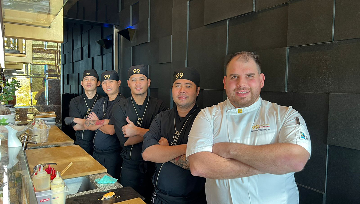 Sushi brigade in black uniforms behind their head chef in a dark kitchen