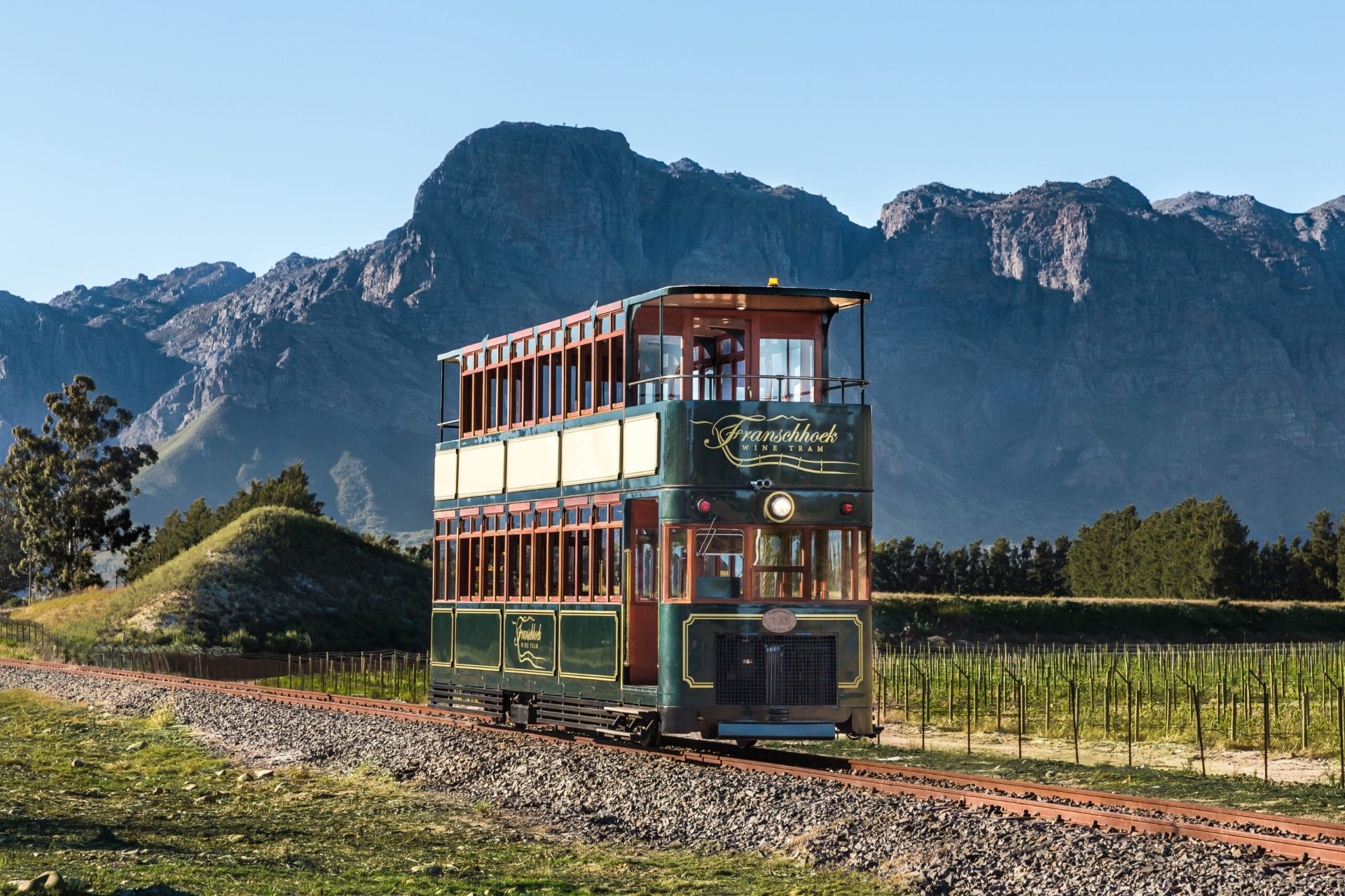 Vintage Franschhoek wine tram on the rails with the granite mountains rising behind it